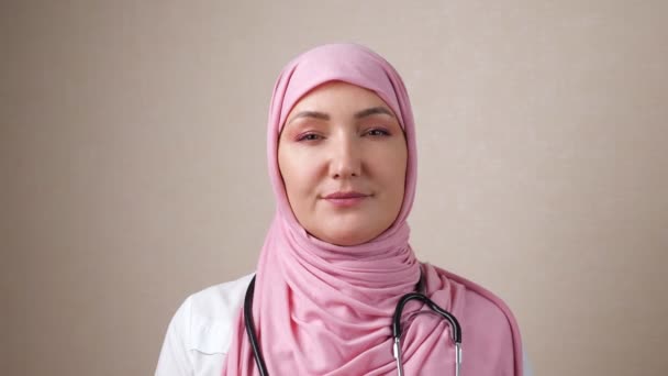 Γυναίκα γιατρός σε μαντίλα με φωνοενδοσκόπιο στο λαιμό χαμογελώντας κοιτάζοντας την κάμερα — Αρχείο Βίντεο