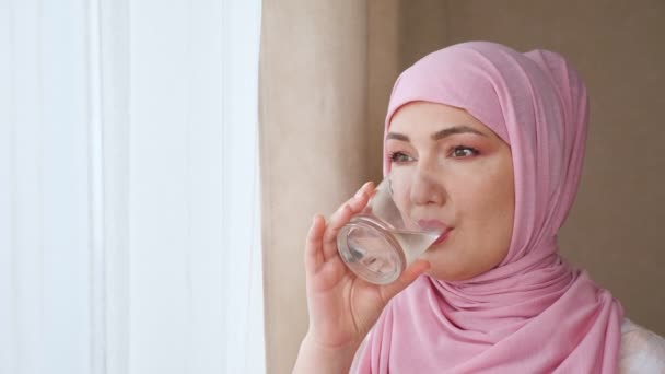 Νεαρή γυναίκα με μαντίλα πίνει νερό από ποτήρι. — Αρχείο Βίντεο