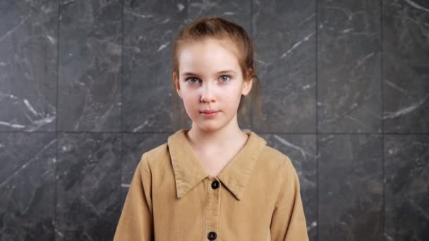 Rolig skolflicka i brun jacka ser rakt och ler — Stockvideo