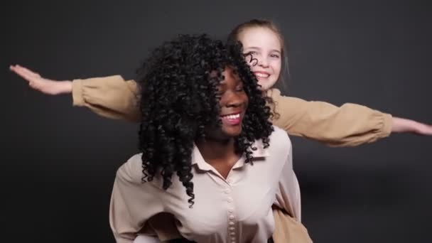 Stylish black stepmother holds adopted schoolgirl on backs — Stock Video