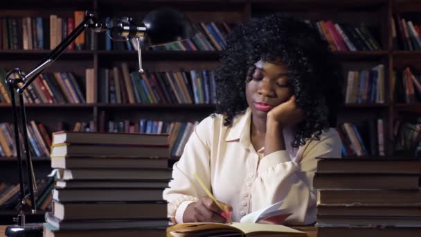 Афроамериканська жінка пише за столом у напівтемній кімнаті. — стокове відео