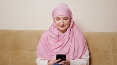 Tesettürlü genç bir kadın telefonda gülümsüyor.