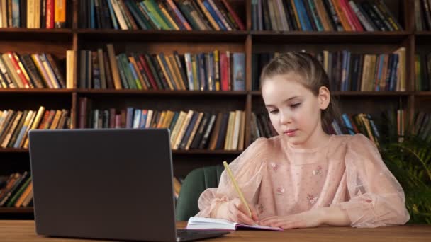 Девушка смотрит на экран ноутбука и пишет в блокноте — стоковое видео
