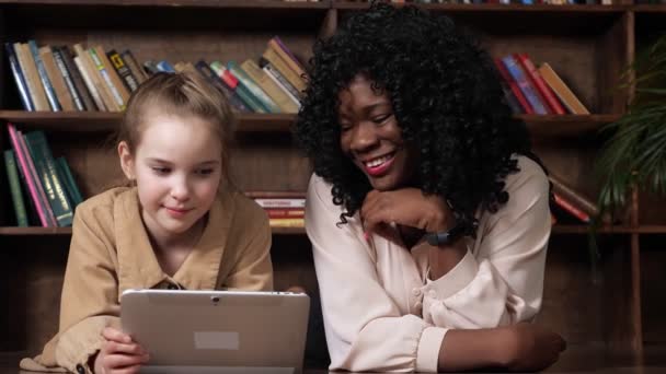 Czarna dama z kręconymi włosami patrzy na tablet wyświetlany przez dziewczynę — Wideo stockowe