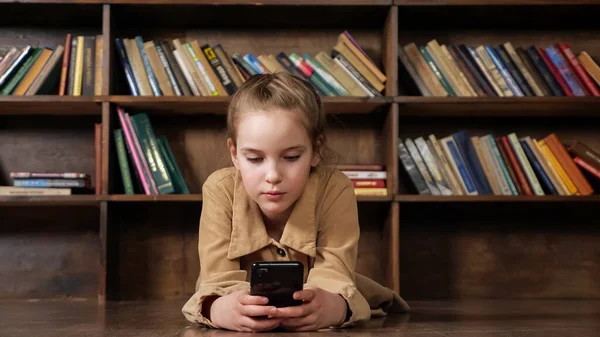 Junior student in bruin jasje speelt spel op smartphone — Stockfoto