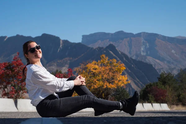 Güneş gözlüklü genç kadın dağlara karşı bariyerde oturuyor.