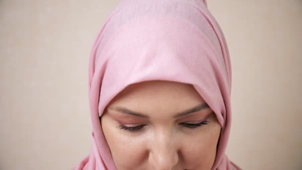 Мусульманка в розовом платке поднимает голову и улыбается, глядя в камеру, замедленная съемка — стоковое видео