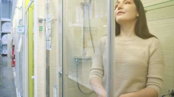 Woman inspecting shower stall with clear glass and silver profile in store — Stock Video