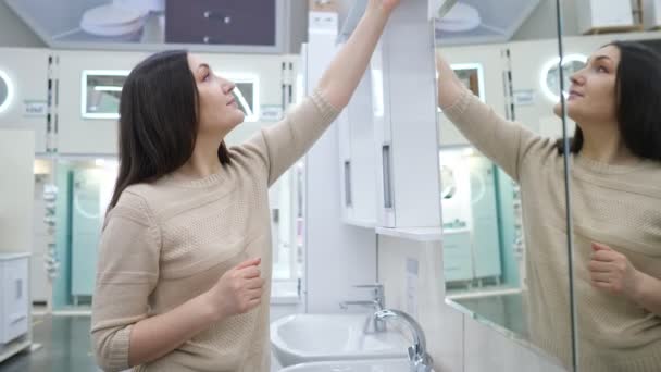 Жінка оглядає дзеркальну шафу з підсвічуванням у ванні в магазині — стокове відео