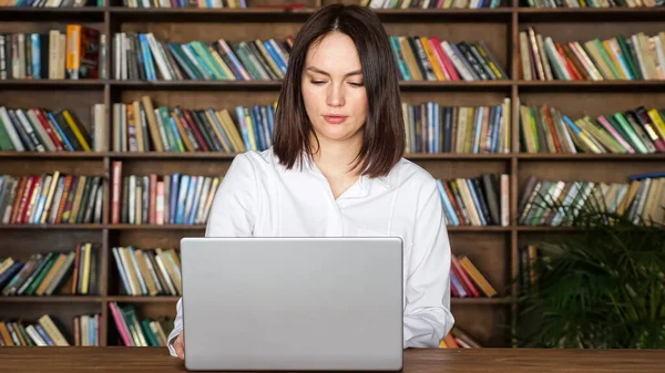 Молода жінка працює з паперами ноутбуком за столом у бібліотеці — стокове фото