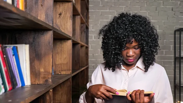 Cheerful African-American woman takes book from wooden shelf