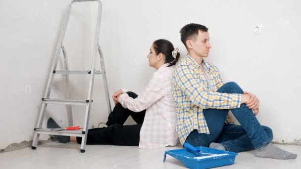 Depressed woman and guy sit near white wall of new apartment — Stock Video