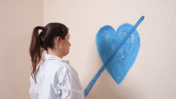 Brune en colère avec des cheveux en queue de cheval traverse le cœur sur le mur — Video