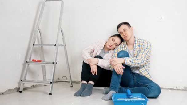 Casal cansado senta-se na parede do apartamento novo branco perto da bandeja — Vídeo de Stock