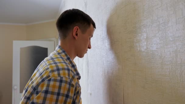 Deprimerad kille i rutig skjorta träffar rummets vägg med huvud — Stockvideo