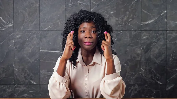 Worried black lady holds crossed fingers of trembling hands — Stock Photo, Image