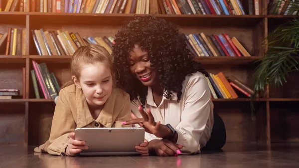 곱슬머리의 흑인 여성 이 소녀의 태블릿 화면을 들여다보고 있다 — 스톡 사진