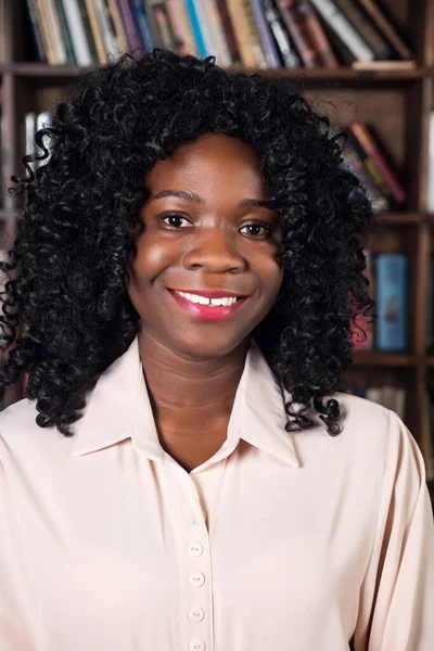 Porträtt av en afrikansk amerikansk kvinna i en blus på bakgrunden av hyllor med böcker — Stockfoto