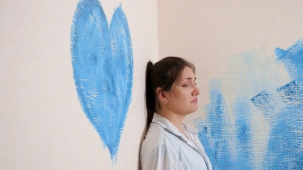 Depressieve brunette huilt in de buurt van muur met blauw hart — Stockvideo