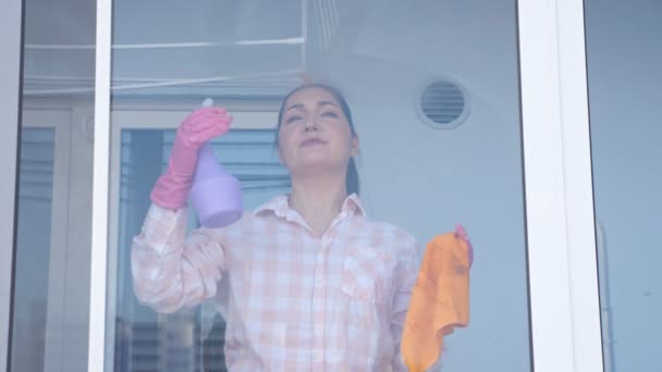 Молода жінка миє вікно в рукавичках з ганчіркою, зовнішній вигляд, повільний рух — стокове відео