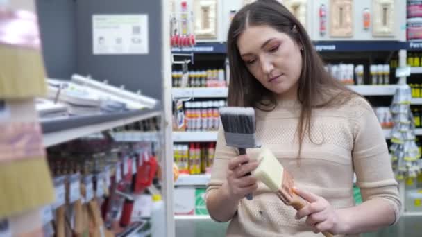 İnşaat malzemeleri dükkanında boya fırçası seçen genç bir kadın. — Stok video