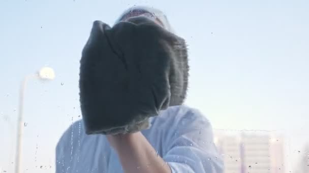 Ung kvinna i scarf tvättar fönstret, suddig bakgrund — Stockvideo