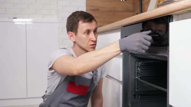Mannen kontrollerar trasig ugn för att reparera sittning på golvet i köket — Stockvideo