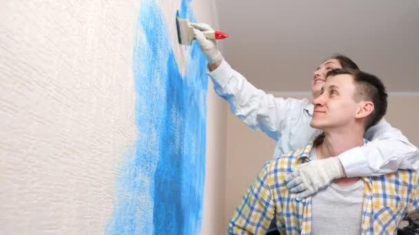 Guy tiene fidanzata sulla schiena mentre la signora dipinge muro in blu — Video Stock