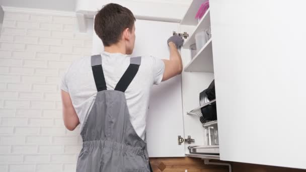 Ремесленник устанавливает дверцу шкафа на современной кухне — стоковое видео