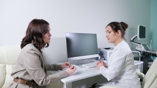 Az orvos köntösben hallgatja a beteget az asztalnál számítógéppel — Stock videók
