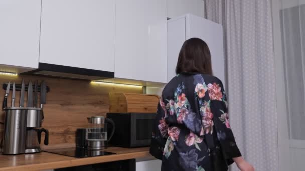 Mujer en bata se cuela hasta el refrigerador grande para tomar pastel — Vídeos de Stock