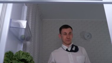 Gömlekli sarhoş adam buzdolabını açar ve soğuk bira alır.