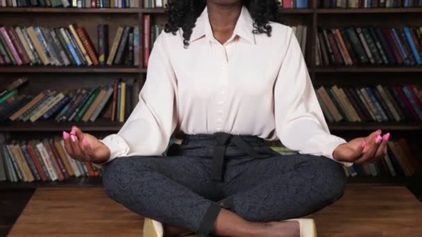 Zwart vrouw in wit blouse zit in yoga pose lotus op tafel — Stockvideo