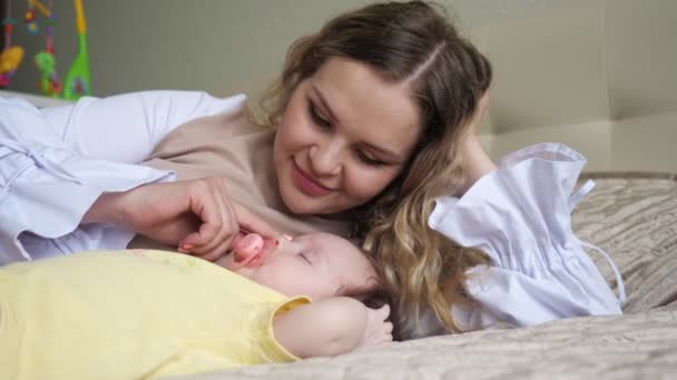 Joyful jovem mãe encontra-se na cama grande perto de bebê menina — Vídeo de Stock