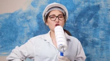 Miğferli genç kadın mikrofon gibi şarkı söylüyor.