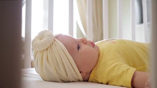 Playful baby girl in yellow clothes lies in bassinet closeup — Stock Video