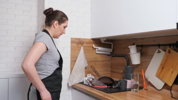 Αναστατωμένη γυναίκα έρχεται στην κουζίνα και βλέπει βρώμικα πιάτα στο νεροχύτη — Αρχείο Βίντεο