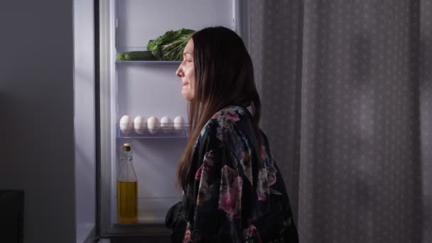 Silueta ženy jíst eclair v ledničce v tmavé kuchyni — Stock video