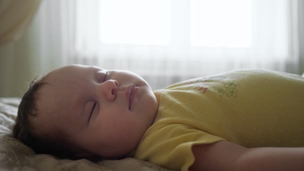 赤ちゃん女の子で黄色服睡眠でベッドに対して窓 — ストック動画