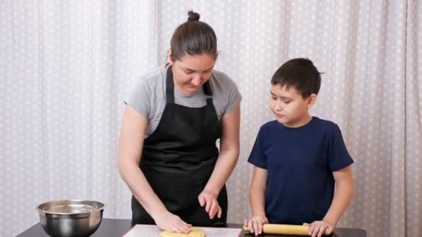 Boy rolls out the dough under the supervision of a woman — Stock Video