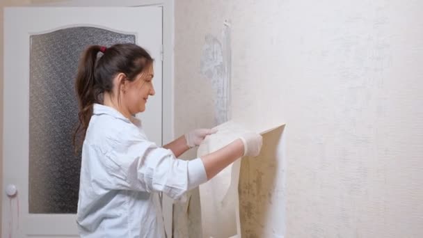 Lächelnder Wohnungsbesitzer mit Pferdeschwanz nimmt alte weiße Tapeten — Stockvideo