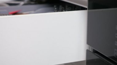 Closing white drawer of kitchen cabinet full of utensils