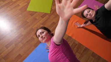 Young women in t-shirts practice yoga exercises on mats