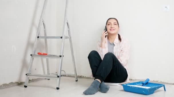 Señora nueva propietaria del apartamento se sienta apoyada en la pared vacía blanca — Vídeos de Stock