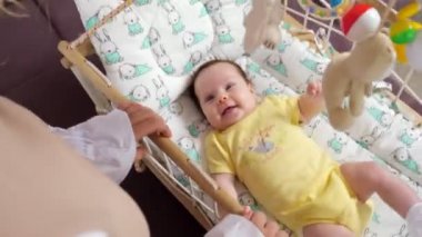 Tanınmayan bir kadın sallanan yatakta neşeli bir çocuğu sallıyor.