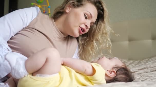 Radostná matka s volnými kudrnatými vlasy hraje s dítětem na posteli — Stock video
