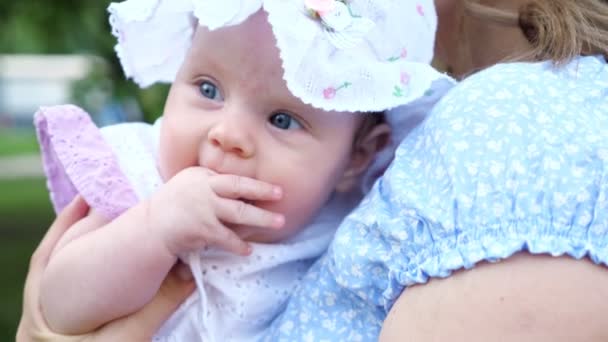 Дитяча дівчинка з блакитними очима дивиться навколо сидячи в руках матері — стокове відео