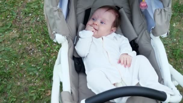 Engraçado criança pequena em macacão branco encontra-se em carruagem de bebê cinza — Vídeo de Stock