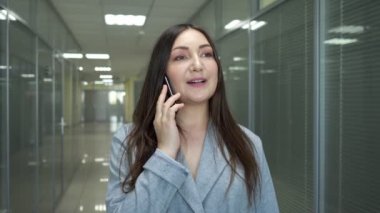Gri ceketli esmer iş kadını akıllı telefondan konuşuyor.