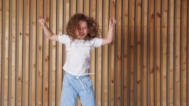 Niña preescolar con el pelo largo y suelto rizado salta sonriendo — Vídeos de Stock